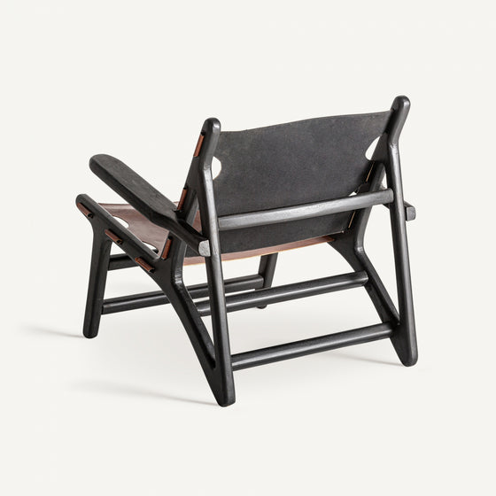 El Sillón Bourthes de madera de mango y piel es una silla de madera negra con una estructura geométrica única y un asiento de cuero marrón, que evoca un estilo vintage. Se muestra desde atrás sobre un fondo blanco liso.