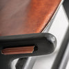 Primer plano de un apoyabrazos de estilo vintage en el Sillón en madera de mango y piel Bourthes, que muestra un acabado de metal negro con detalles de cuero marrón y desgaste visible como rayones y una pequeña área expuesta.