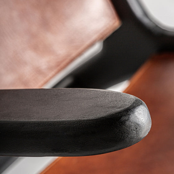 Primer plano de un apoyabrazos negro en el Sillón en madera de mango y piel Bourthes con cuero marrón, resaltando su estilo vintage y su textura intrincada.