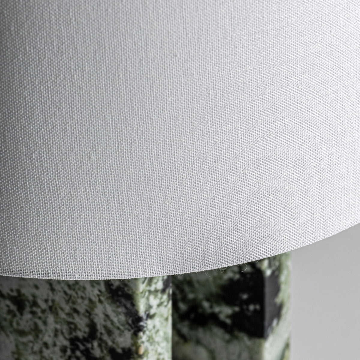 Primer plano de la pantalla blanca texturizada de la Lámpara de mesa en mármol Verdea, con una base estampada en verde y negro visible debajo: un toque elegante para una iluminación elegante inspirada en el art déco.