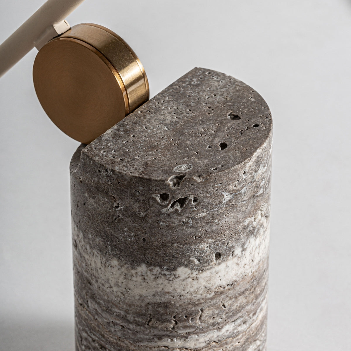 La lámpara de mesa en bronce y mármol Yzara combina un disco de bronce sobre una base cilíndrica de mármol gris con capas visibles y pequeños orificios, creando un diseño art déco perfecto para aportar calidez a tu espacio.