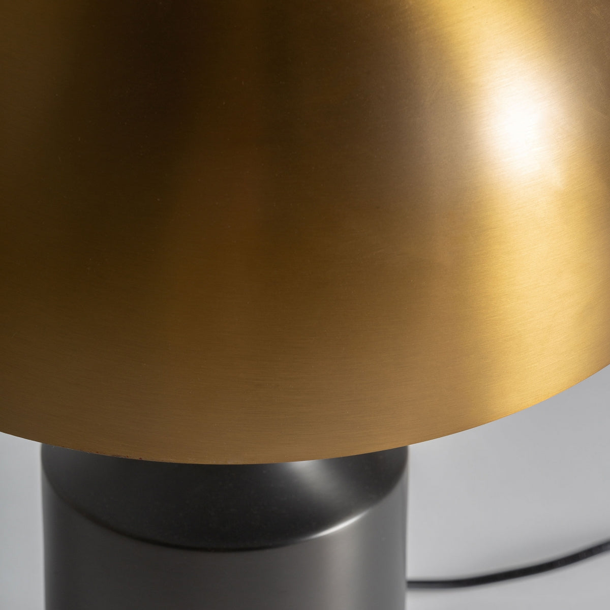 Primer plano de la Lámpara de mesa en bronce Aterra, mostrando su diseño Art Decó con una base cilíndrica negra mate y una pantalla en forma de cúpula de color dorado metálico.