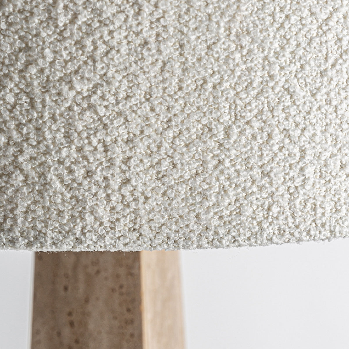 Primer plano de una pantalla texturizada de color blanco roto con una vista parcial de la base de la lámpara de mesa Tetbury en bronce y mármol en tonos de madera claros sobre un fondo liso.