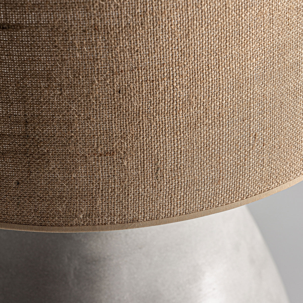 Primer plano de la Lámpara de mesa en terracota y yute Min, que presenta una pantalla de yute beige texturizada sobre una base lisa de color gris claro.
