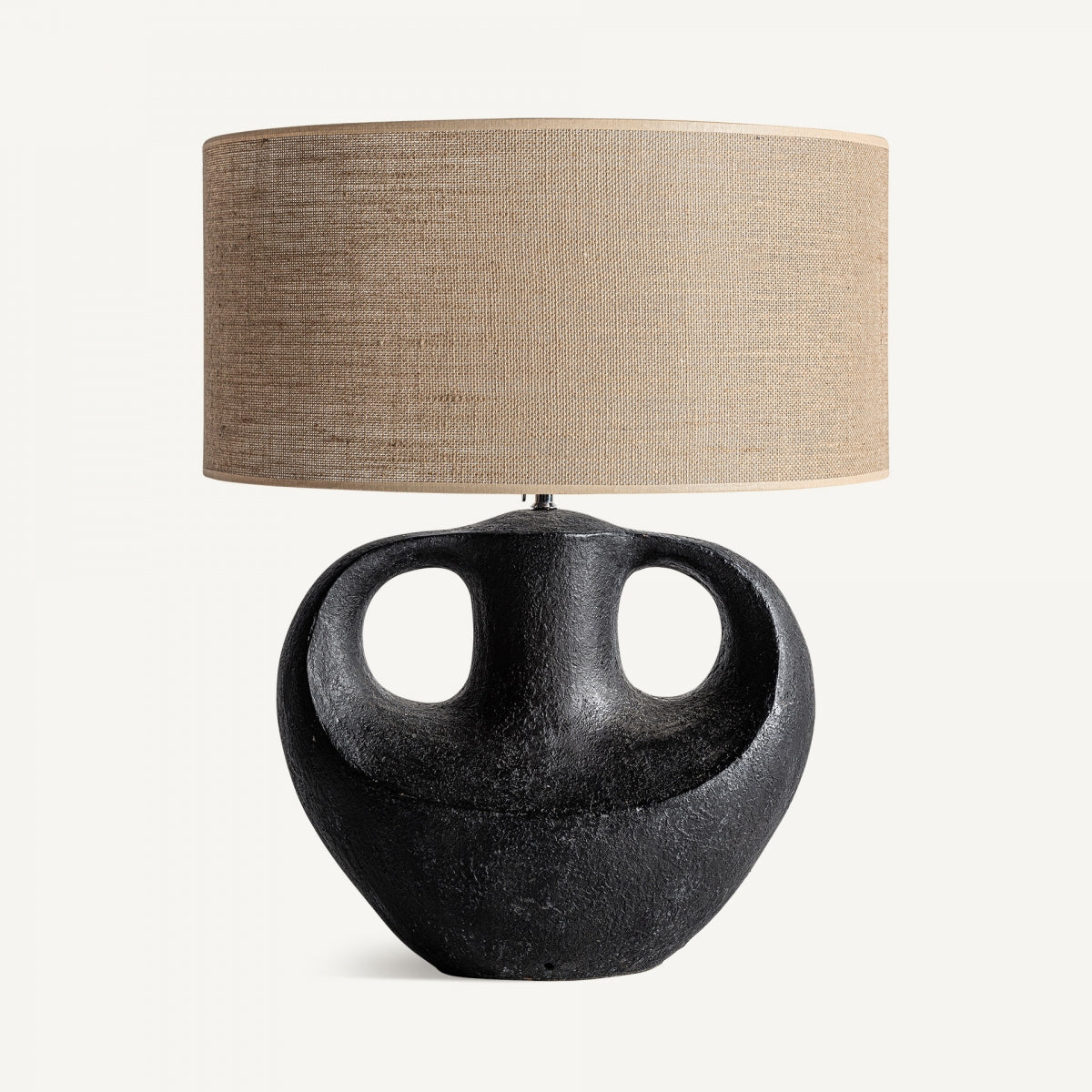 La lámpara de sobremesa en terracota y yute Froda presenta una base de terracota texturizada negra mate con dos orificios recortados y una gran pantalla cilíndrica de tela de yute beige.