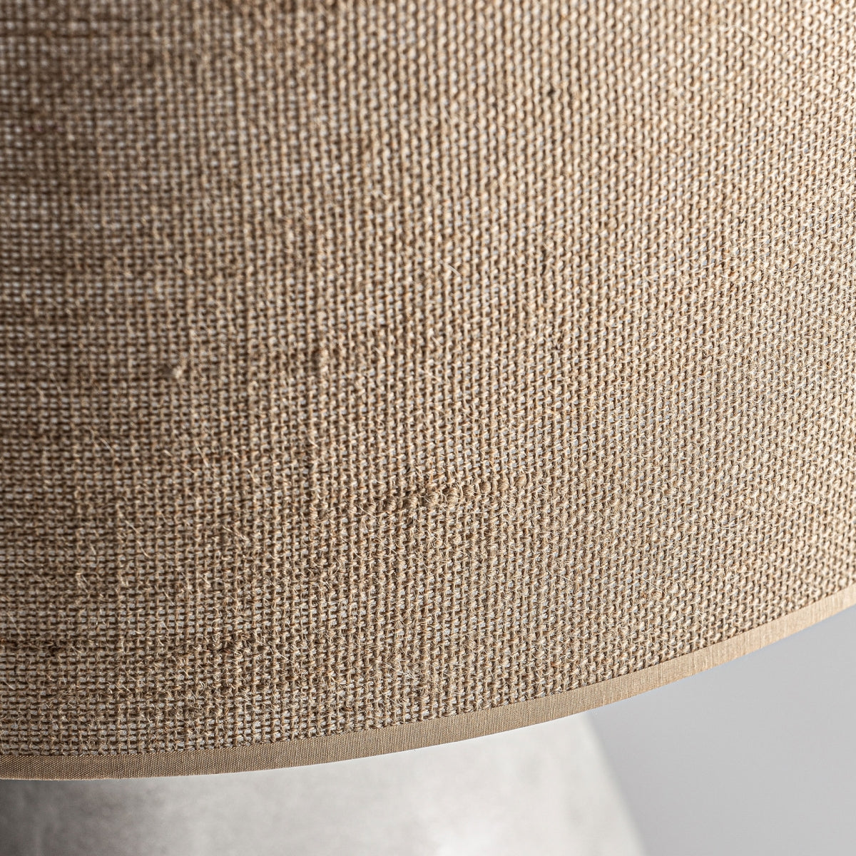 Primer plano de la pantalla de yute texturizado de color beige de la Lámpara de sobremesa en terracota y yute Froda, con una pequeña parte de su base de color claro visible en la parte inferior.