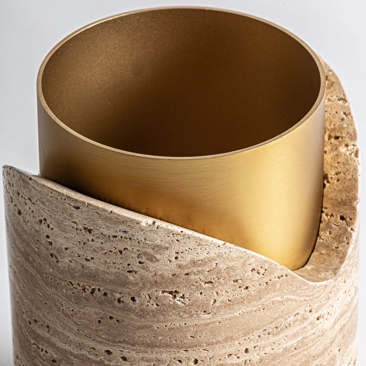 El Jarrón en mármol y acero Verkie G presenta un jarrón cilíndrico de metal dorado colocado en un soporte de mármol crema con un corte diagonal y un elegante diseño art déco, que se muestra sobre un fondo blanco liso.