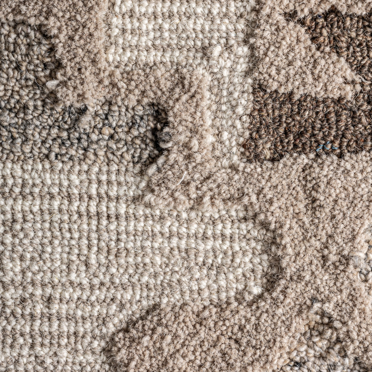 Primer plano de una alfombra texturizada beige y marrón con desgaste visible, ideal para un diseño boho o para combinar con el Cuadro decorativo de algodón beige y madera de mango (120x90 cm) IVAR.