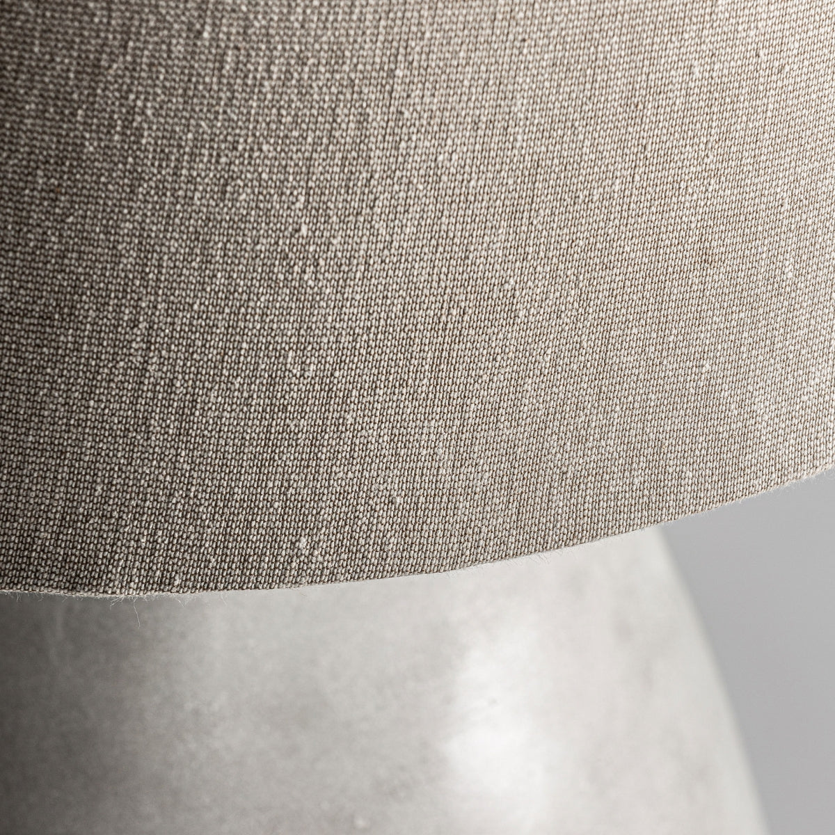 Primer plano de una pantalla de algodón beige con una superficie texturizada encima de la suave Lámpara de mesa en cemento blanco y algodón Seren, perfecta para una decoración contemporánea.