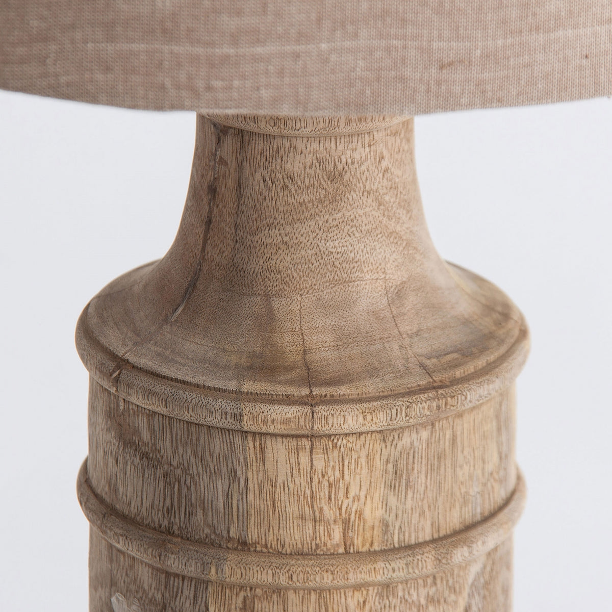 Primer plano de la Lámpara de sobremesa en madera de mango y algodón Lynda, que presenta una base de madera de mango con acabado natural y una pantalla de algodón beige para un estilo clásico y atemporal.