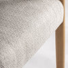 Primer plano de un cojín de tela tejida beige en la silla de comedor de madera de fresno Staple, que resalta la textura y la esquina del asiento. La sutil veta de la madera de fresno realza su elegancia, reflejando un estilo colonial sobrio.