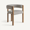 La silla de comedor en madera de fresno Wizerne es una silla moderna con respaldo curvo tapizado y asiento de tela gris, complementado con cuatro patas de madera para un diseño de comedor rústico.