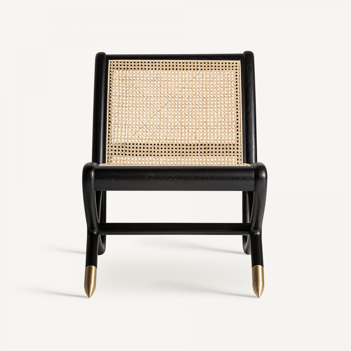 El sillón de madera de fresno y ratán Gladbeck, de madera negra con asiento y respaldo de caña tejida, personifica la decoración bohemia. Sus elegantes patas angulares tienen remates dorados, todo ello sobre un fondo blanco liso.