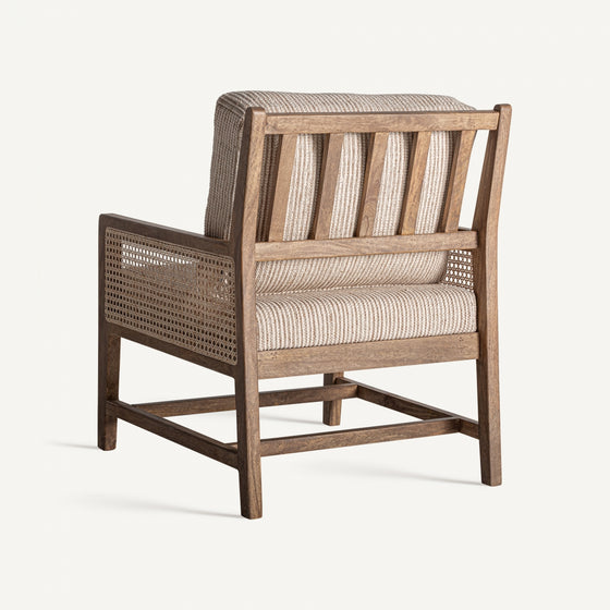 El Sillón en madera de mango y mimbre Romarand es un sillón de madera que presenta un respaldo y asiento de tela acolchada y rayada, acentuado con paneles de mimbre beige tejido en los lados para una elegancia clásica.