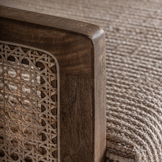 Primer plano de un Sillón en madera de mango y mimbre Romarand con detalles de ratán tejido y una manta de punto beige texturizada sobre él, que irradia elegancia clásica.