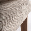 Un primer plano del Sillón en madera de mango y mimbre Romarand resalta su asiento tejido en beige texturizado combinado con patas de madera elegantemente elaboradas.
