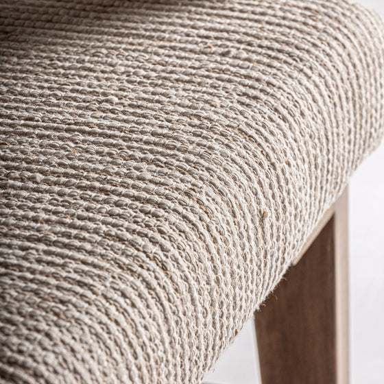 Un primer plano del Sillón en madera de mango y mimbre Romarand resalta su asiento tejido en beige texturizado combinado con patas de madera elegantemente elaboradas.