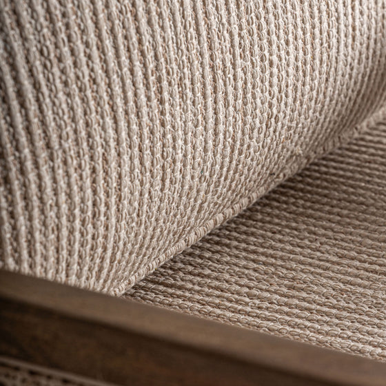 Primer plano del Sillón en madera de mango y mimbre Romarand, resaltando su elegancia clásica con tela tejida beige y marco de madera, mostrando texturas y fibras detalladas.