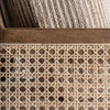 Primer plano de una cesta de mimbre Romarand con un patrón tejido que recuerda a la elegancia clásica y que contiene una manta texturizada de color beige.