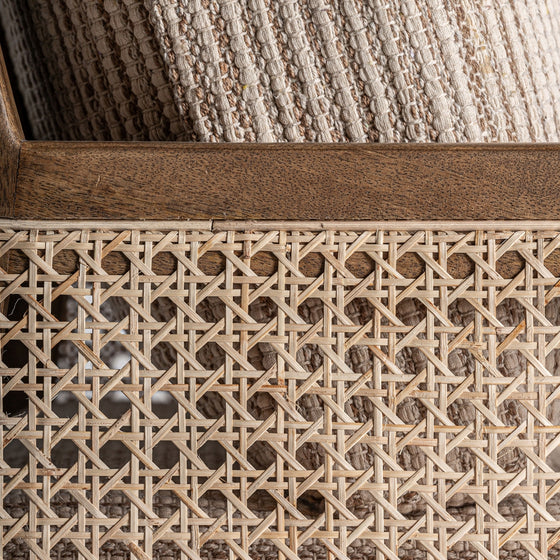 Primer plano de una cesta de mimbre Romarand con un patrón tejido que recuerda a la elegancia clásica y que contiene una manta texturizada de color beige.