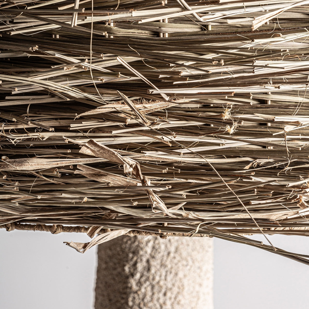 Un primer plano de hierba seca apretada forma la base de la Lámpara de pie en resina y hierba Nyland, que presenta una forma cilíndrica rugosa de color beige, ideal para la decoración moderna.