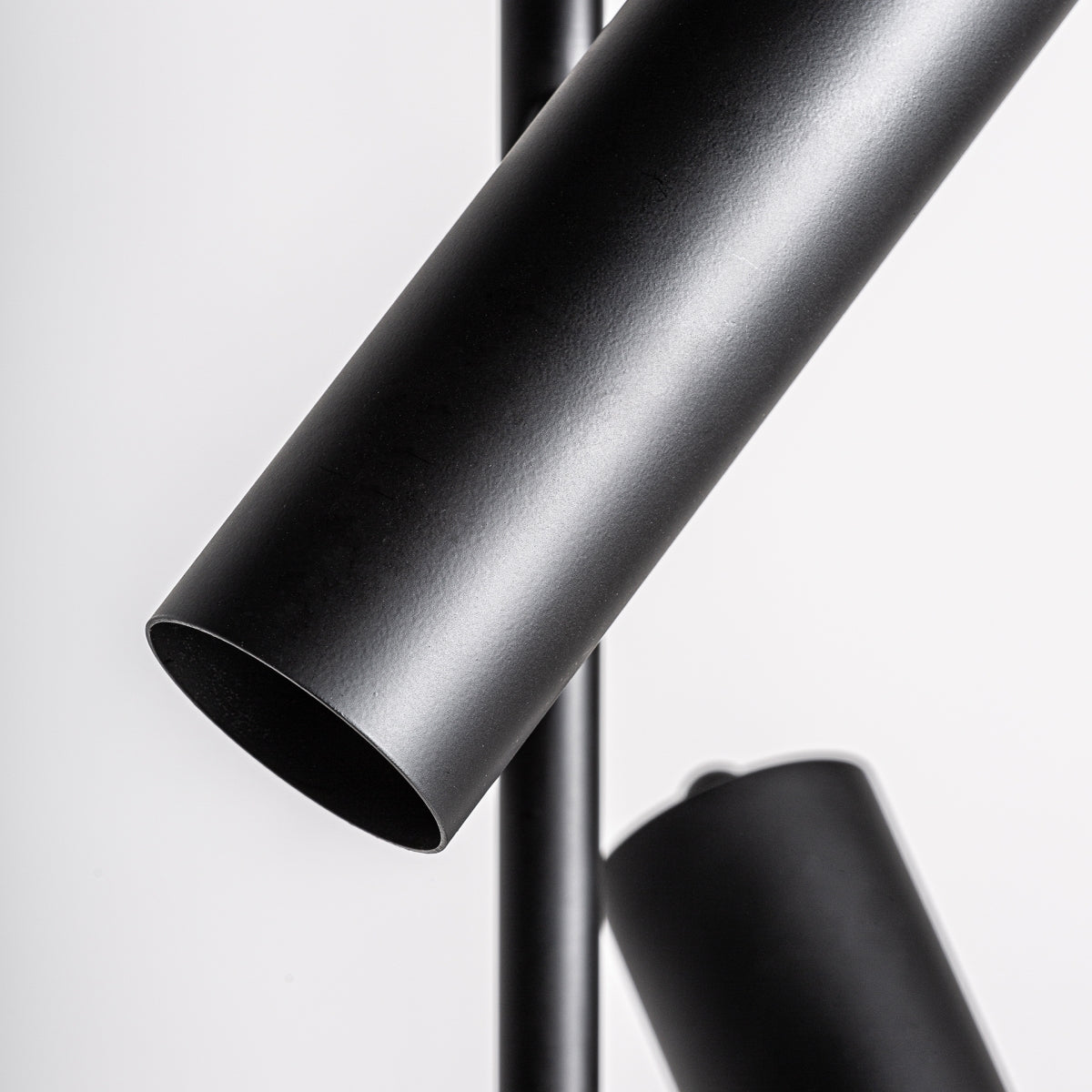 Primer plano de la Lámpara de pie en hierro y mármol Deco, que muestra dos tubos de metal negro que se cruzan sobre un fondo blanco, inspirado en el estilo art déco, ideal para iluminación de calidad.