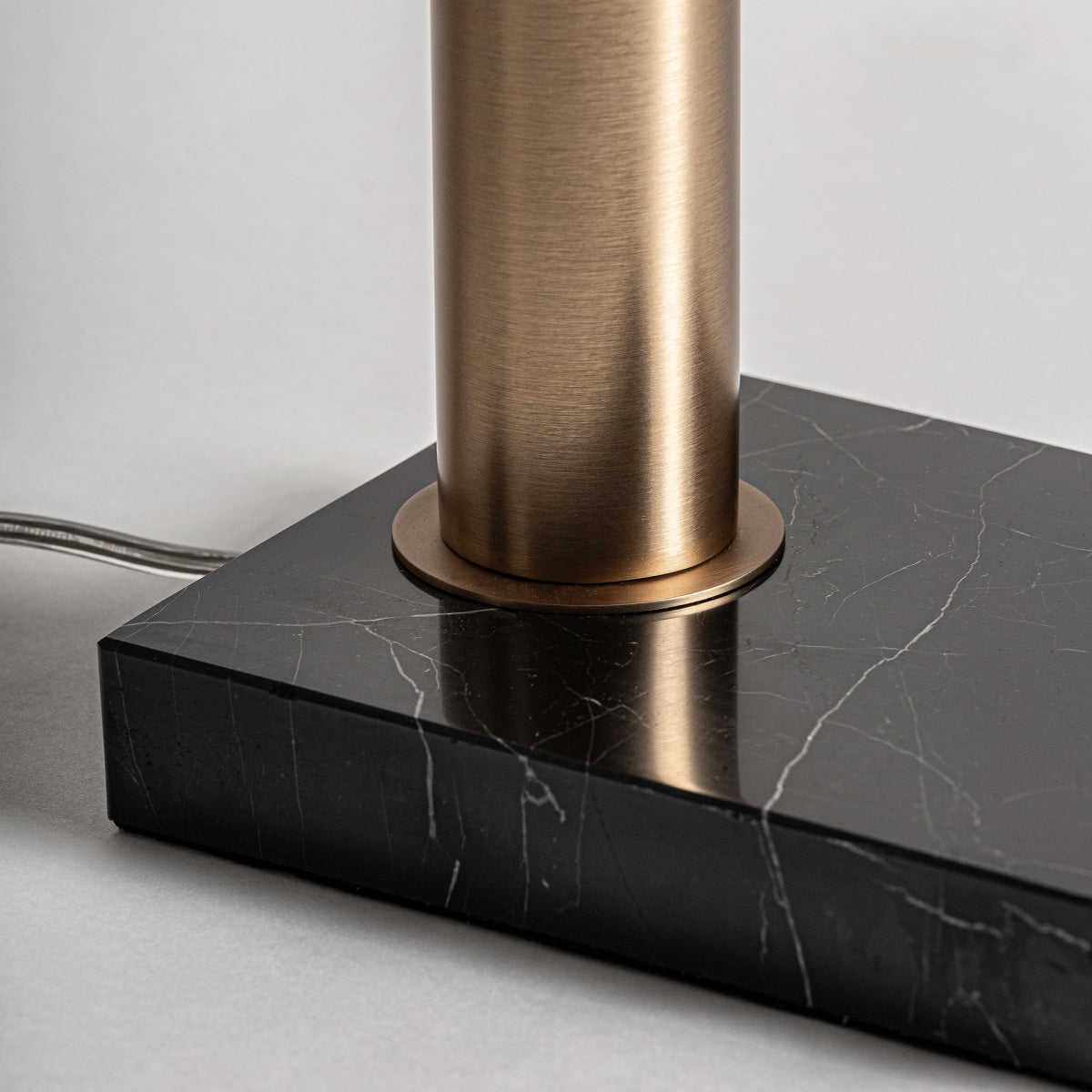 Detalle en primer plano de la base cilíndrica de la lámpara de pie en hierro y mármol Arte, montada sobre una losa rectangular de mármol negro con vetas blancas, estilo Art Decó. El cable eléctrico sale desde la base.