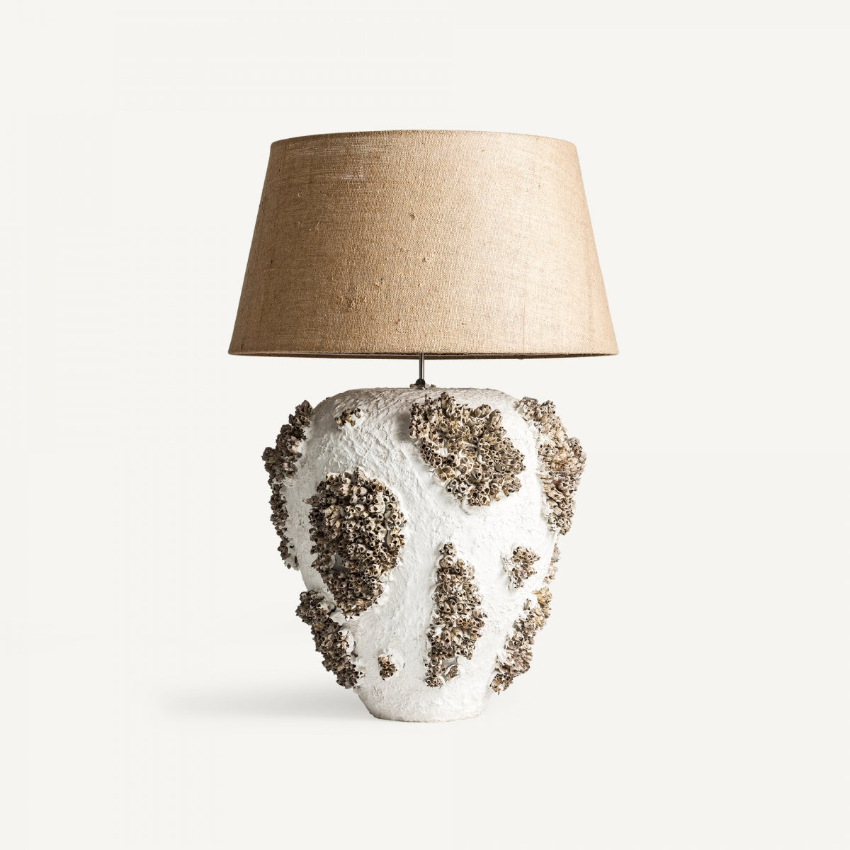 La lámpara de mesa Thora, con una base de terracota blanca con manchas oscuras que recuerdan al coral y una pantalla de yute beige, personifica el diseño moderno a la vez que proporciona una iluminación cálida.