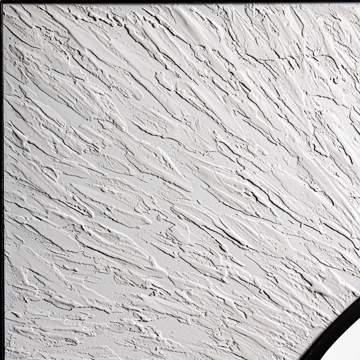 Pared de yeso blanco texturizado con una esquina del Espejo redondo en madera y hierro (100x100 cm) Hakim visible en la parte inferior derecha, mostrando patrones lineales en relieve a lo largo de su superficie.