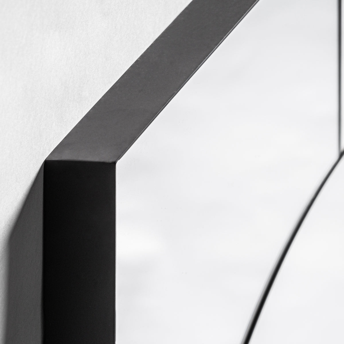 Primer plano de la esquina del Espejo art déco en madera y hierro negro (61x91 cm) Ferdi, que cuenta con un marco negro y refleja la luz sobre una pared blanca para realzar la luminosidad en cualquier espacio.