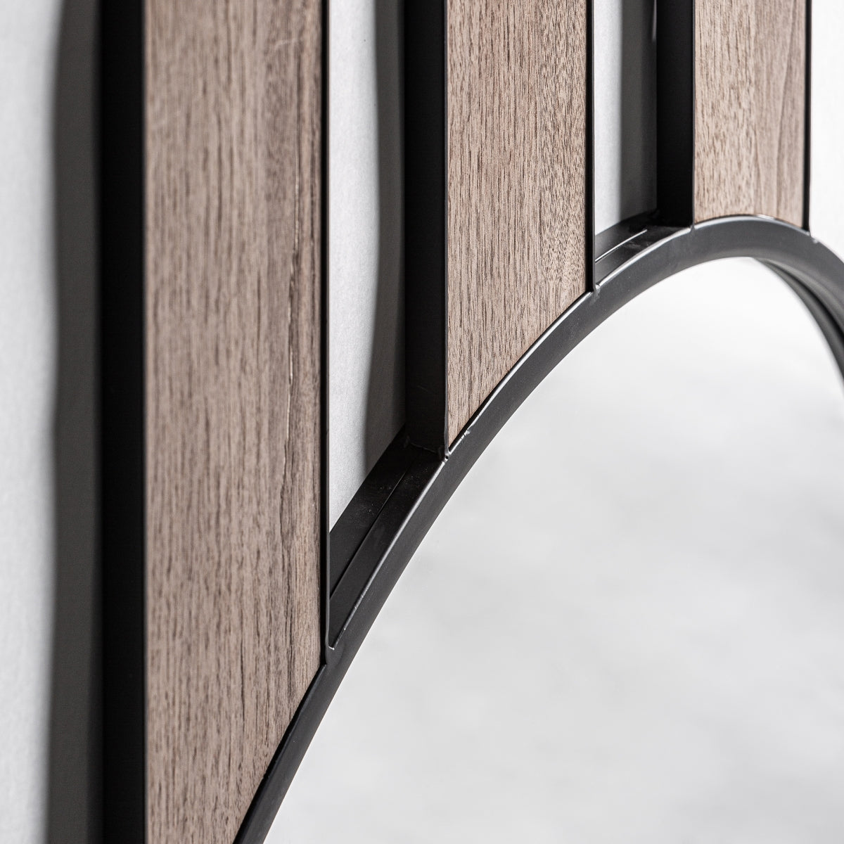 Primer plano del Espejo de pared en madera y hierro (80x222 cm) Finbar, con un marco curvo de metal negro y detalles verticales en madera, ideal para ampliar espacios y realzar la decoración de interiores sobre un fondo difuminado.