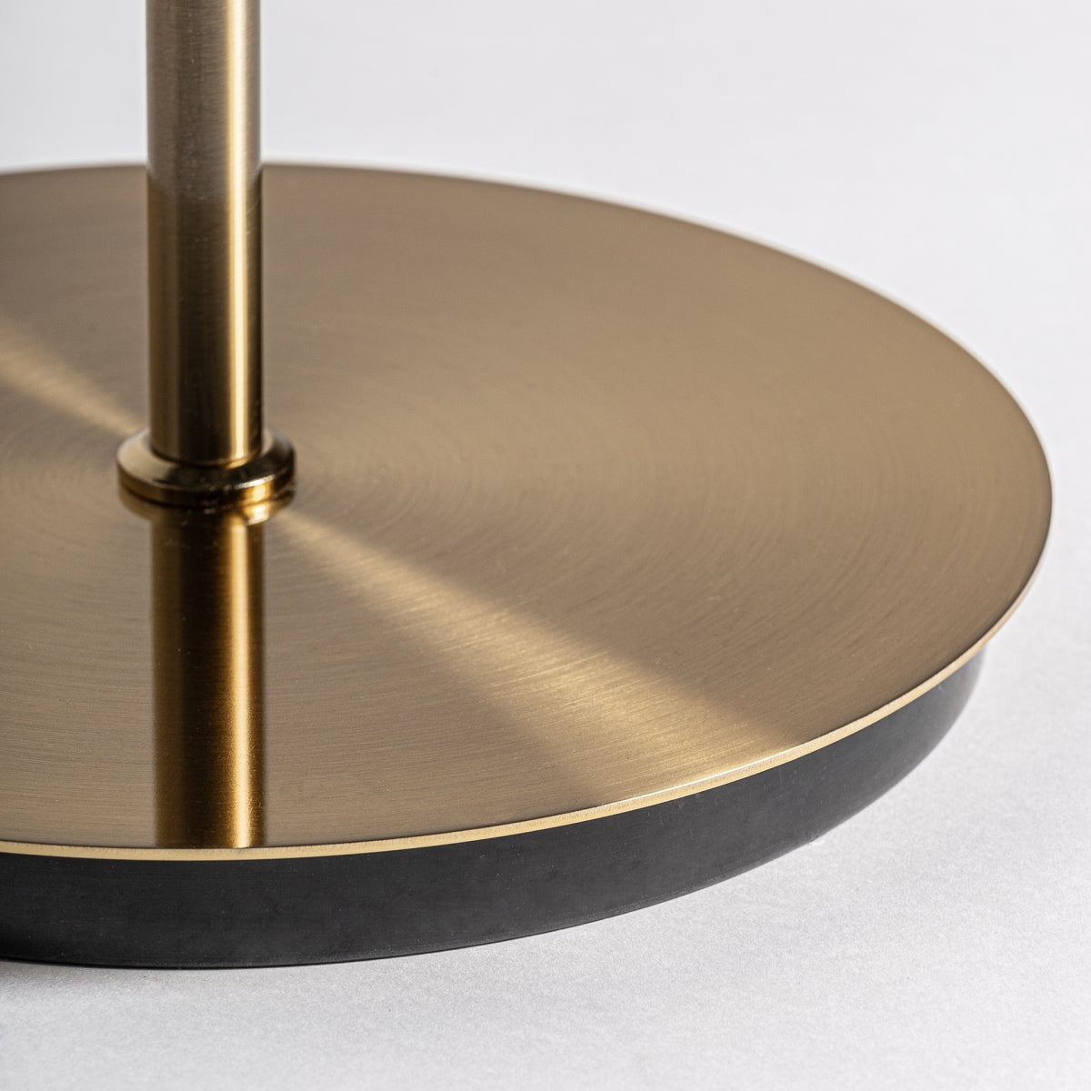 Primer plano de la base redonda de latón cepillado de la Lámpara de pie en metal cristal y acrílico Arte 16, que presenta un delgado poste vertical, colocado sobre una superficie gris claro.
