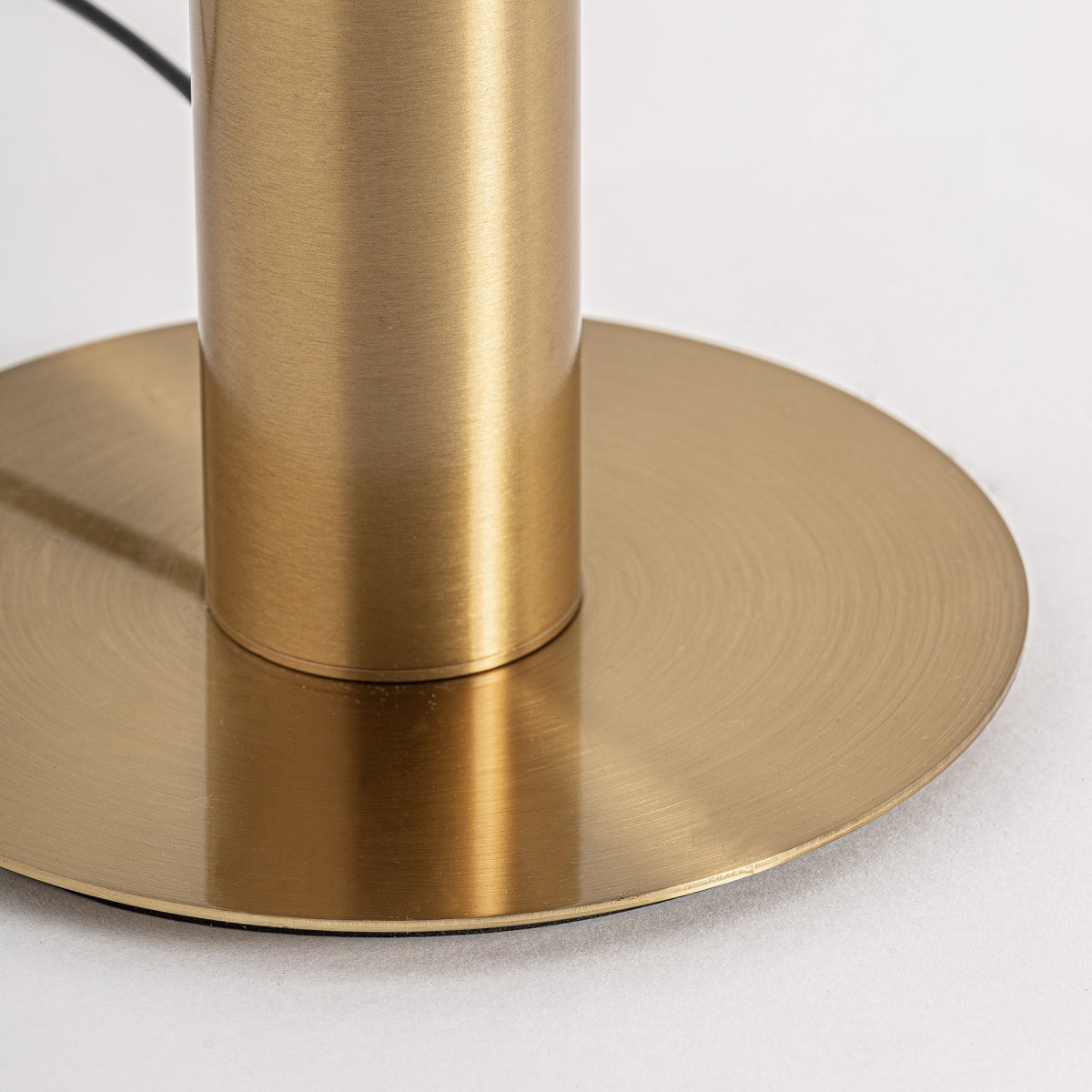 Primer plano de la Lámpara de sobremesa en cristal ahumado Vigo, que presenta un cuerpo cilíndrico de metal con acabado en latón cepillado sobre una base circular, reflejando el estilo art déco y los materiales de primera calidad propios de una elegante lámpara de sobremesa.