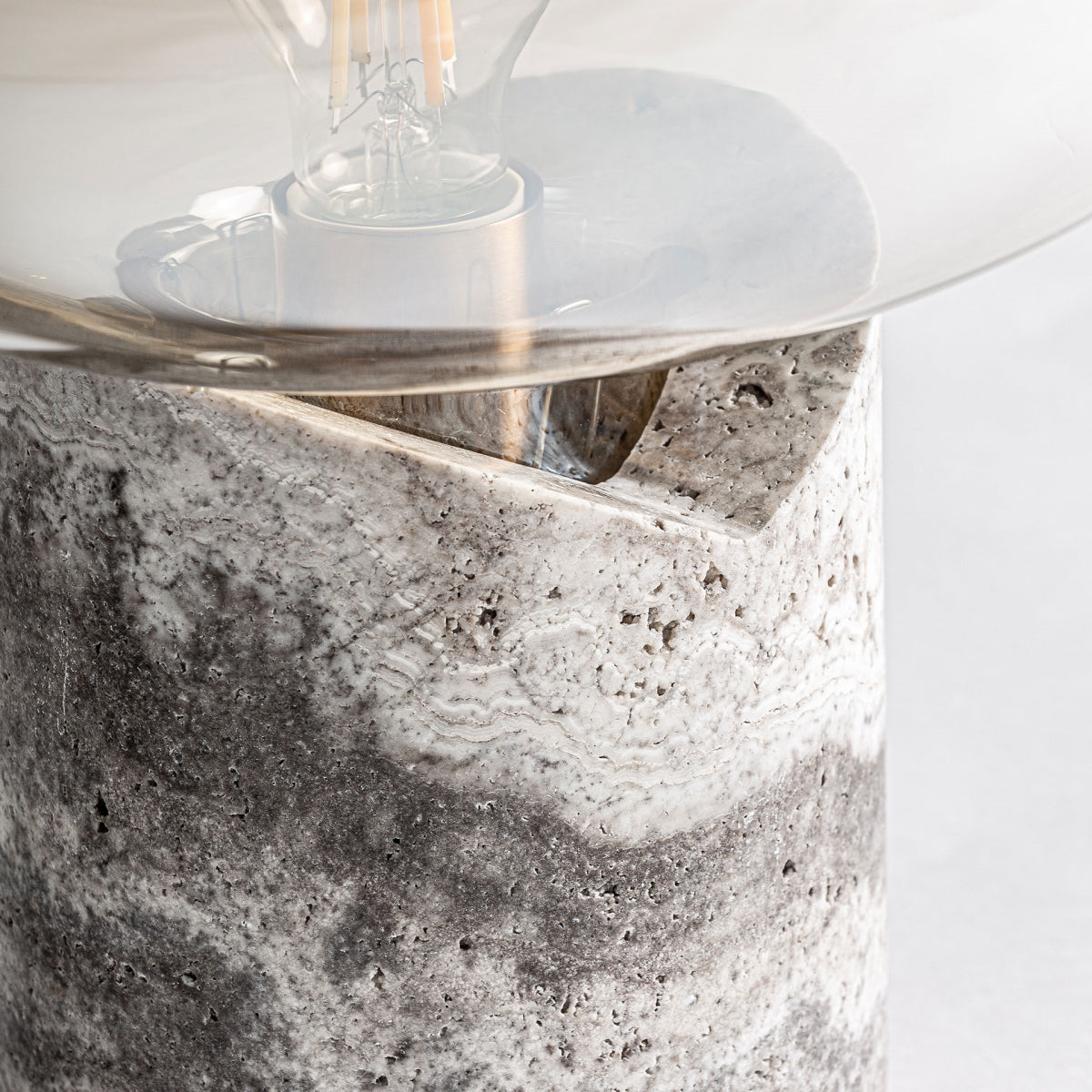 Primer plano de la Lámpara de sobremesa en mármol y cristal Sklo con foco transparente y base cilíndrica de piedra que presenta patrones de mármol y vidrio gris y blanco, mostrando un elegante diseño Art Decó.