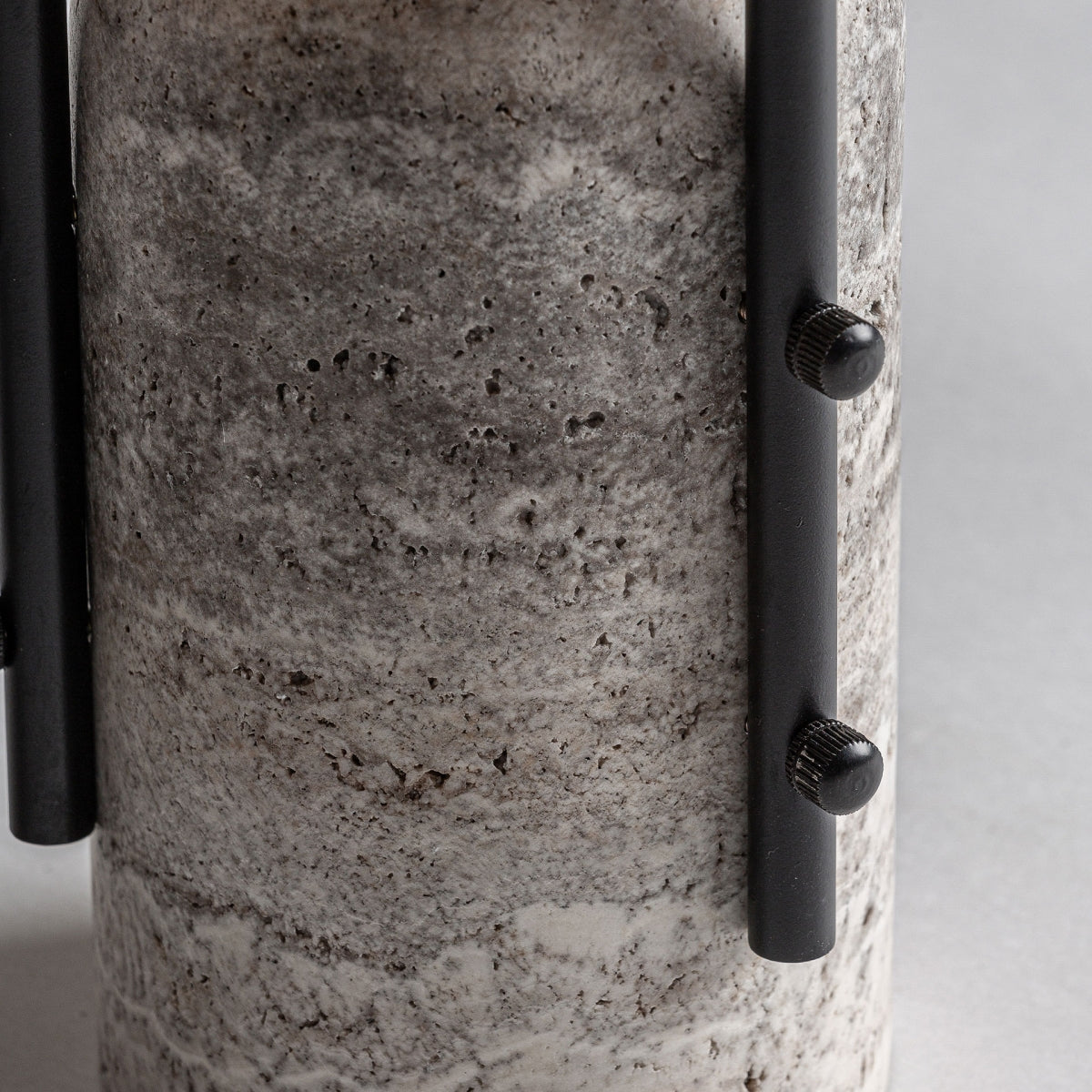 Primer plano de la Lámpara de mesa en mármol y hierro Ind-marbre: una lámpara de mesa cilíndrica con una superficie de mármol gris texturizado y dos varillas de hierro negro unidas mediante tornillos moleteados, que reflejan un toque de diseño art déco.