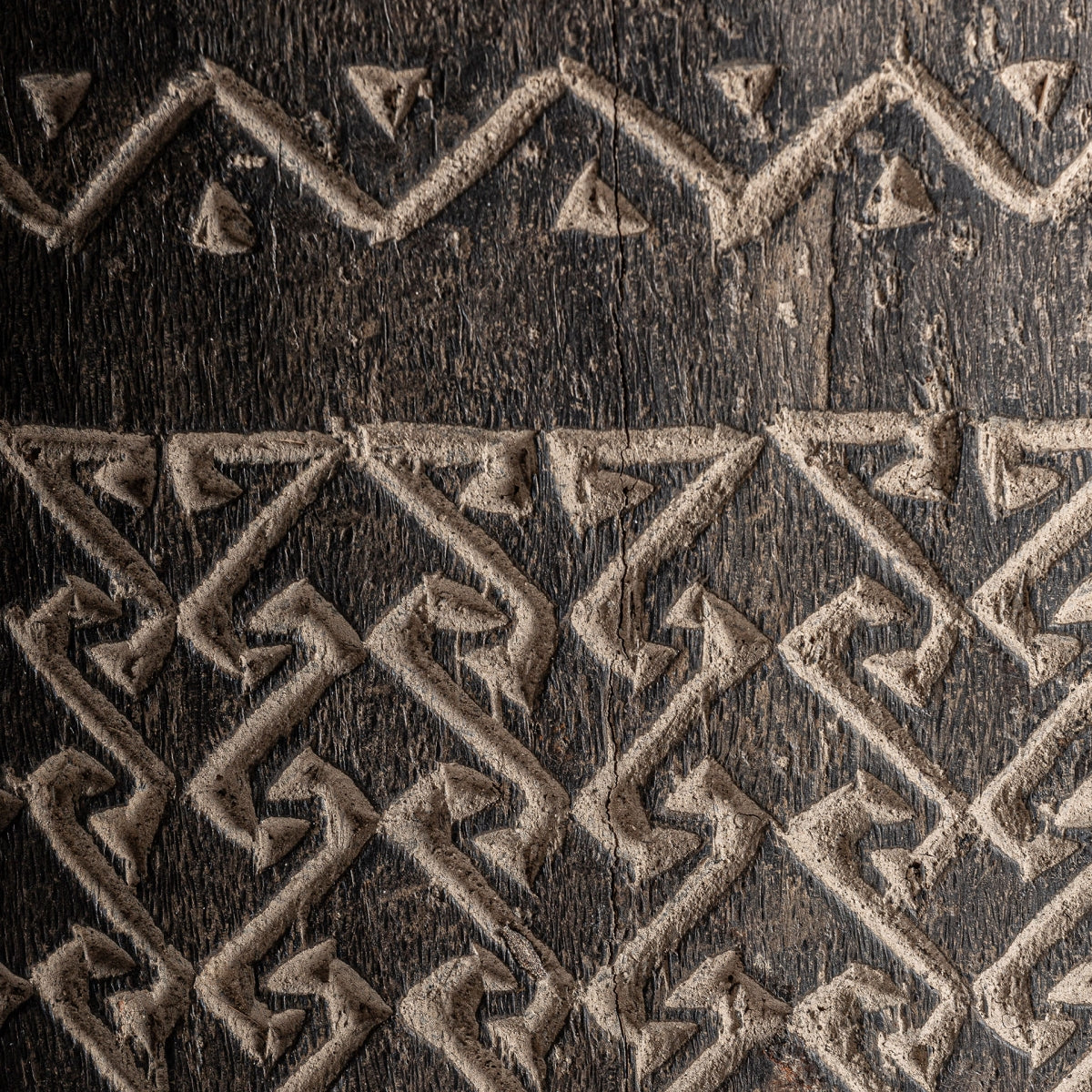Primer plano de superficie de madera texturizada con dibujos geométricos en zigzag y triangulares tallados en el diseño de madera de palma típico de una pieza artesanal como el Jarrón en madera de palma Nantua.
