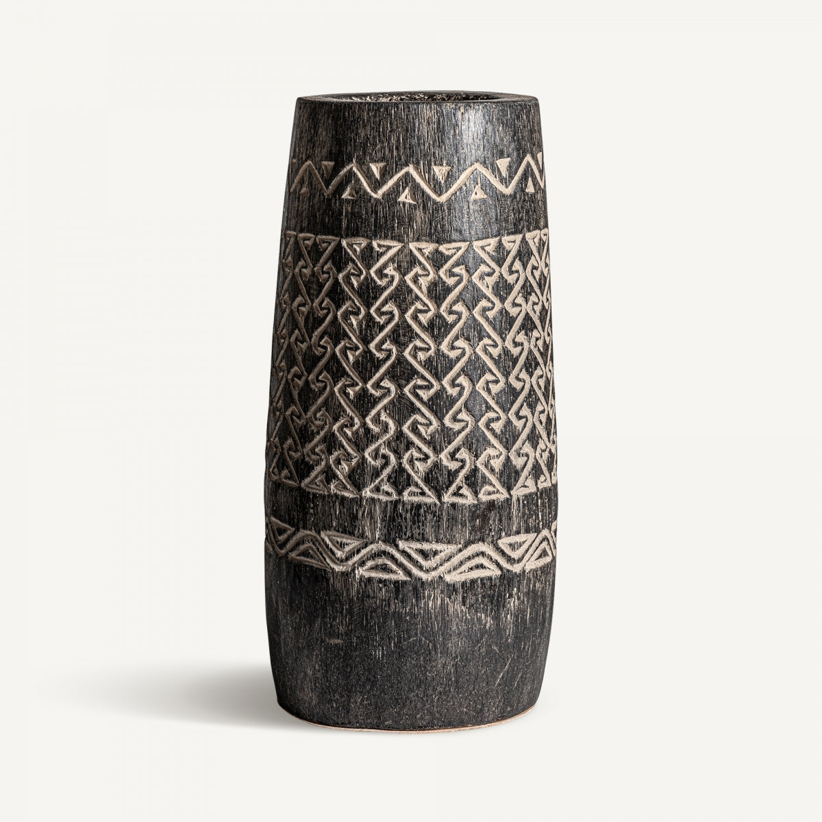 El Jarrón moderno de madera tallada Nantua I es alto, cilíndrico, en negro con patrones geométricos y zigzag blancos grabados, ideal para una decoración exclusiva sobre fondo blanco liso.