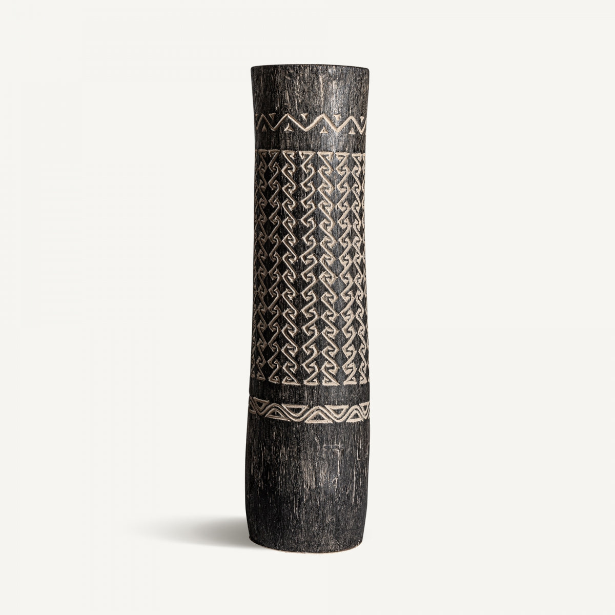 El Jarrón en madera palma tallada Nantua IS es un jarrón cilíndrico alto con patrones geométricos grabados en tonos claros y oscuros, ideal para una decoración contemporánea y bellamente presentado sobre un fondo blanco liso.