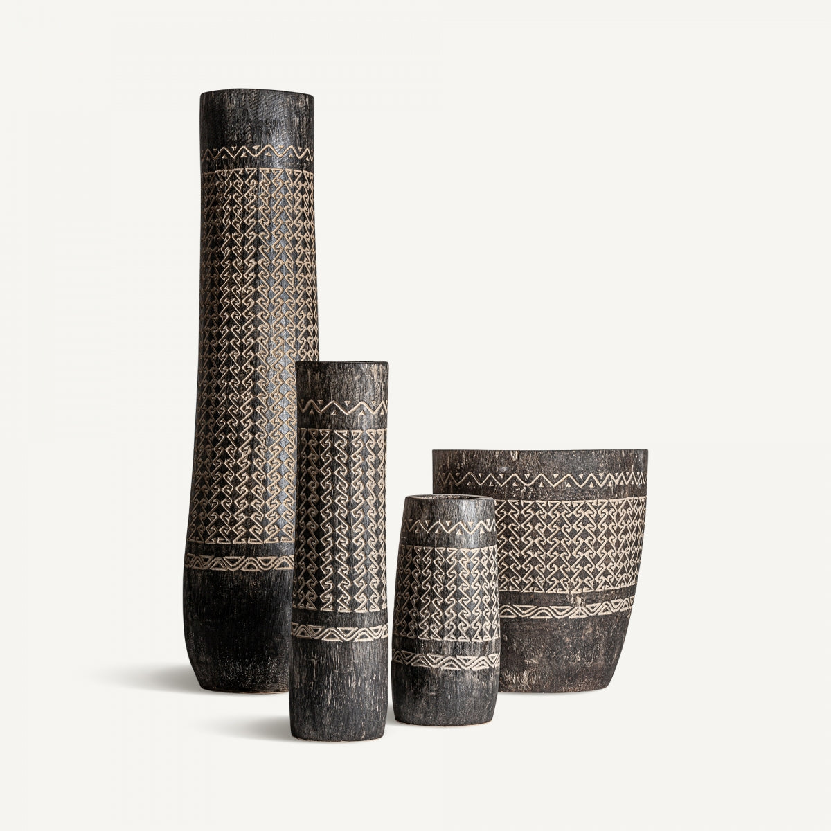 Cuatro jarrones Nantua IS de madera tallada de diferentes alturas con intrincados diseños geométricos se encuentran sobre un fondo blanco liso, añadiendo un toque de decoración contemporánea inspirado en el elegante Jarrón en madera palma tallada Nantua IS.