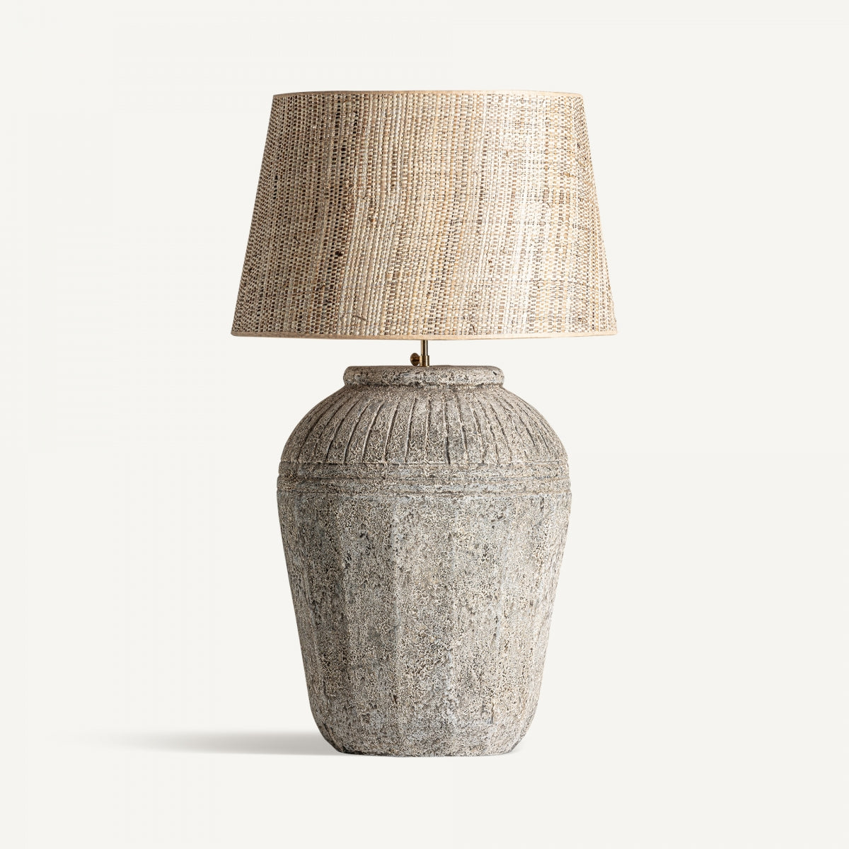 La lámpara de mesa en cerámica gris Siva tiene una textura de piedra y una pantalla tejida en tono neutro, evocando un estilo vintage.