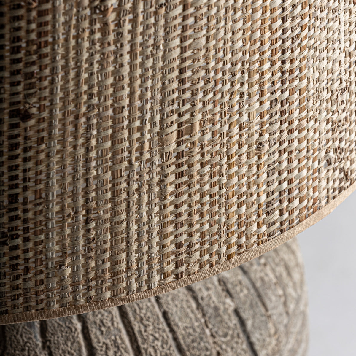 Primer plano de la Lámpara de mesa en cerámica gris Siva, que presenta una pantalla tejida con un aspecto de fibra natural de color beige sobre su base de cerámica gris texturizada, evocando un elegante estilo vintage.