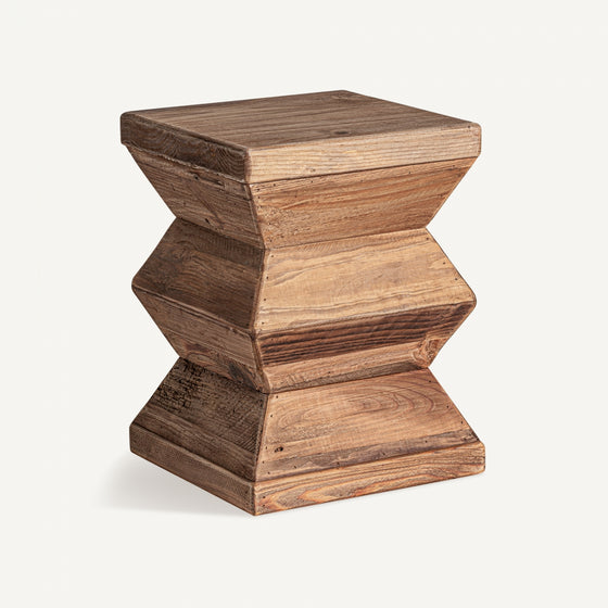 El Taburete bajo Breive presenta una forma de reloj de arena y una textura natural, elaborado meticulosamente por diseño artesanal utilizando madera reciclada con un acabado envejecido.