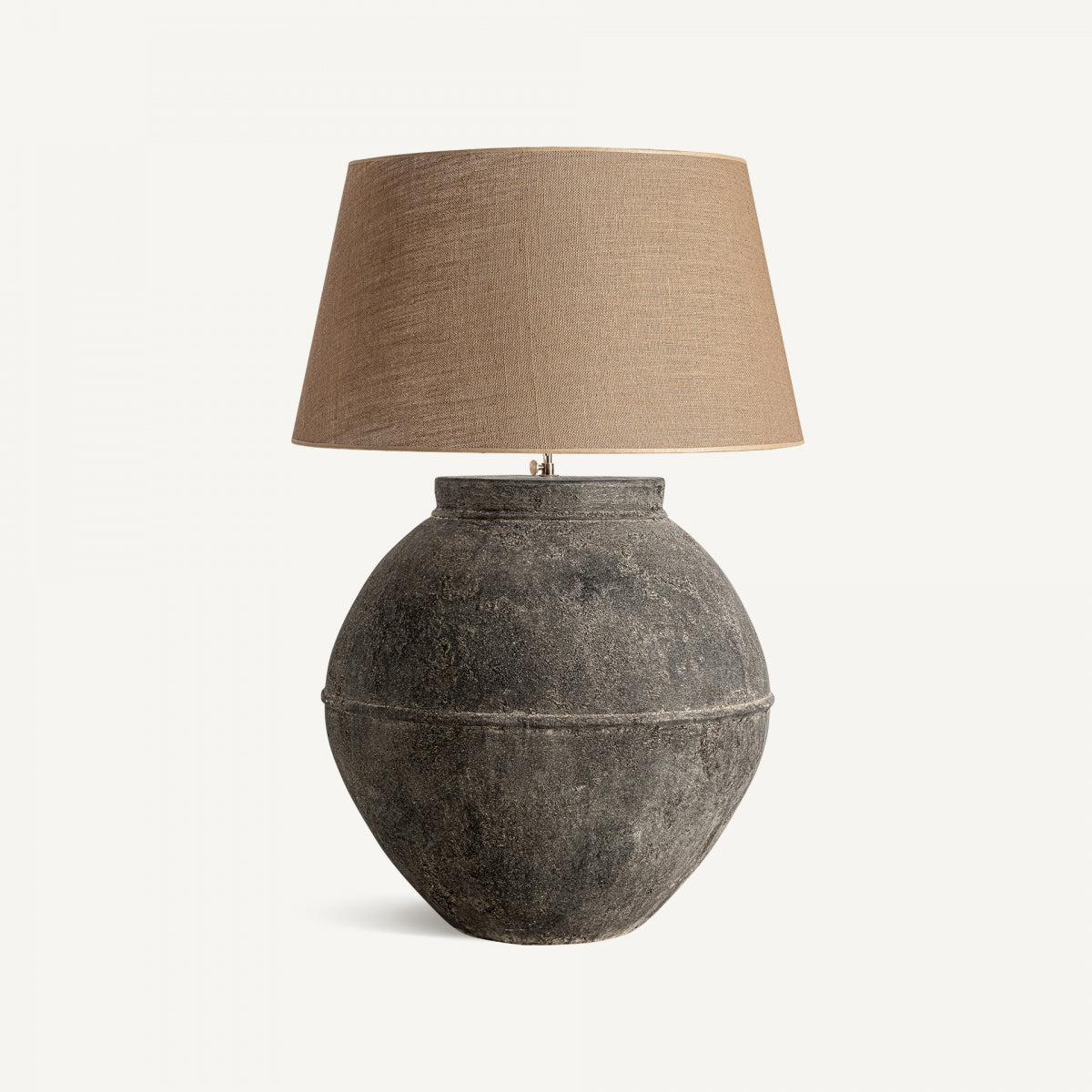 La lámpara de sobremesa de terracota y yute Musia presenta una base redonda de terracota texturizada y una pantalla ancha de yute color canela, perfecta para añadir un estilo contemporáneo a cualquier espacio. Se muestra sobre un fondo blanco liso.