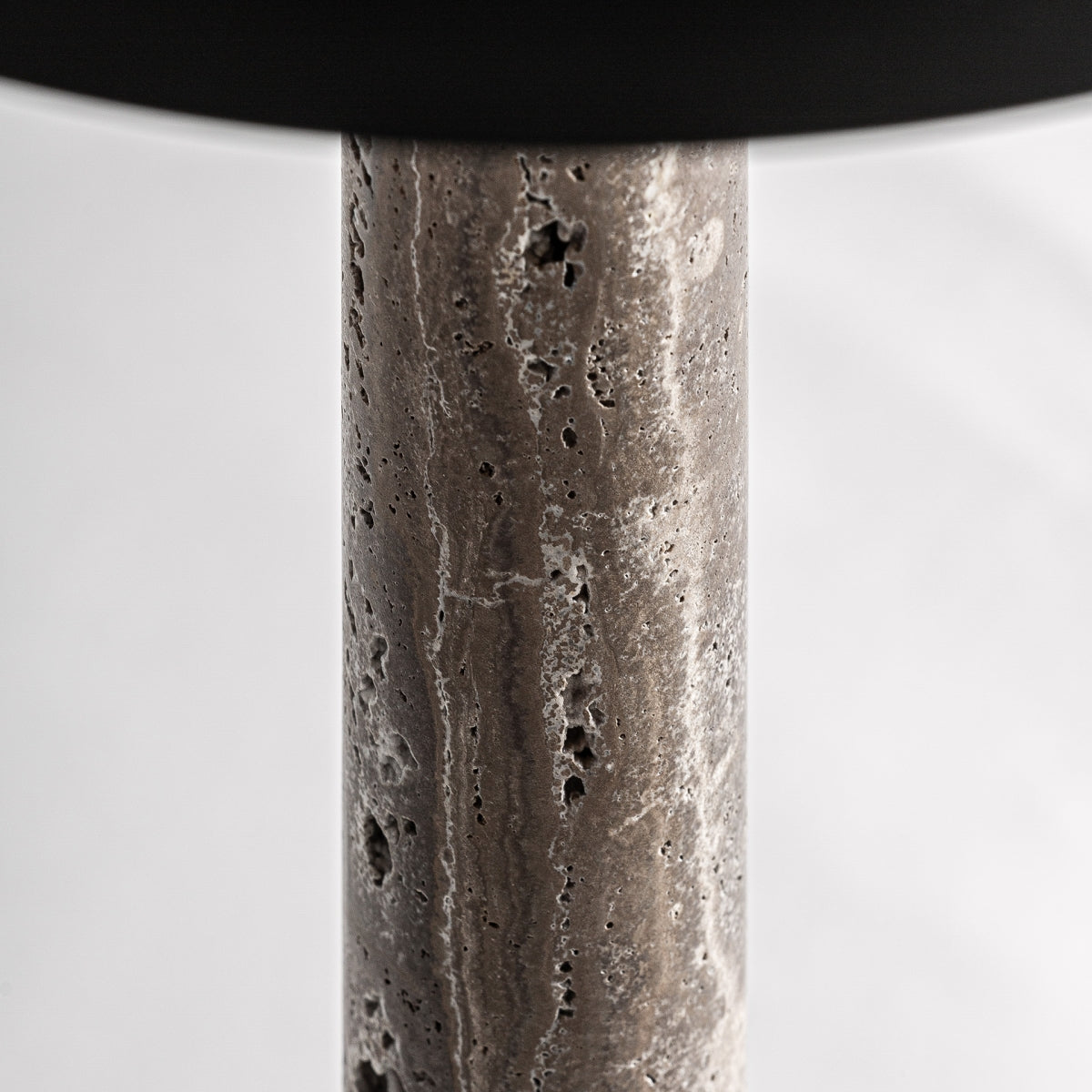 Detalle de la Lámpara de mesa en mármol y metal Sombria, que presenta un cuerpo cilíndrico de mármol con superficie texturizada y pequeños agujeros, destacando su calidad y diseño moderno sobre un fondo sencillo.