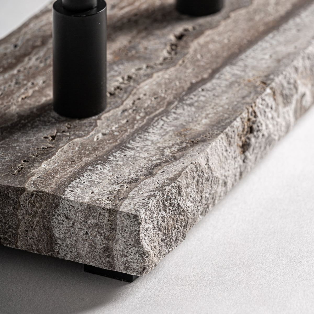 Primer plano de la Lámpara de mesa en mármol gris y metal negro Midcent: una placa de mármol gris texturizada de bordes rugosos con dos varillas de metal cilíndricas negras mate en la parte superior, colocadas sobre una superficie clara.