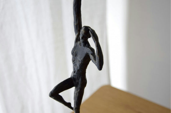 La Figura Decorativa en Bronce y Mármol Horizonte muestra una escultura envejecida de bronce de una figura humana en una pose dinámica y pensativa, con un brazo levantado y el otro doblado sobre el cuerpo. Reposa elegantemente sobre una superficie de madera, invitando a la contemplación.