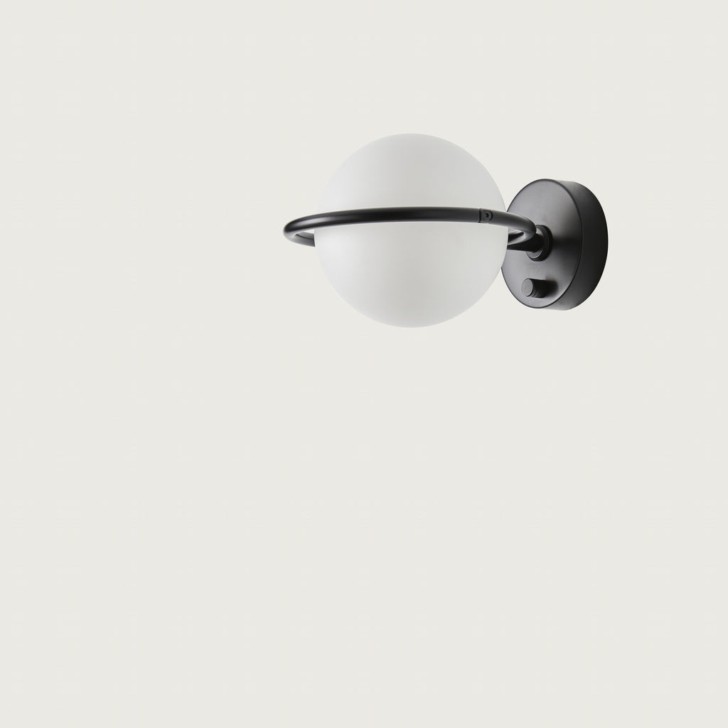 El aplique de pared Abbacus, con pantalla redonda de vidrio esmerilado y aro metálico negro sobre base circular negra, aporta estilo minimalista y diseño sofisticado sobre fondo blanco.