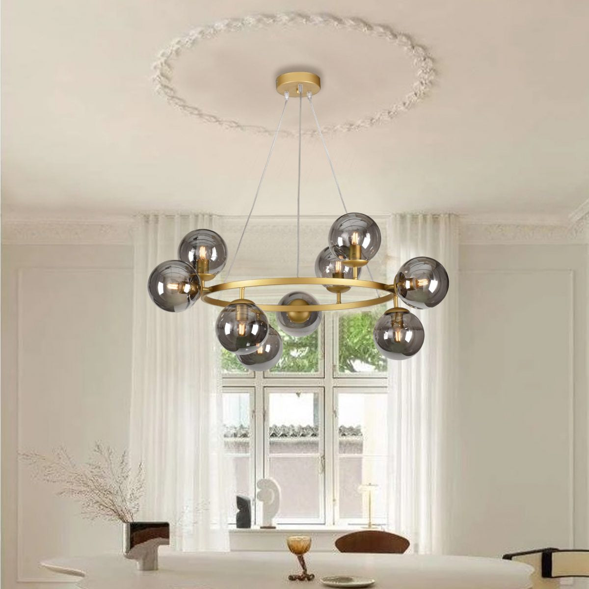 La lámpara de techo de acero esférica C-Ball 9, con múltiples globos de vidrio ahumado para una iluminación uniforme, cuelga sobre una mesa redonda en una habitación de tonos neutros con grandes ventanas y cortinas transparentes.