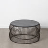 El elegante diseño de la Mesa de centro en metal y mármol plata Novax, con cubierta negra, se destaca sobre un piso de concreto contra una pared blanca nítida, exudando encanto minimalista y sofisticación moderna.