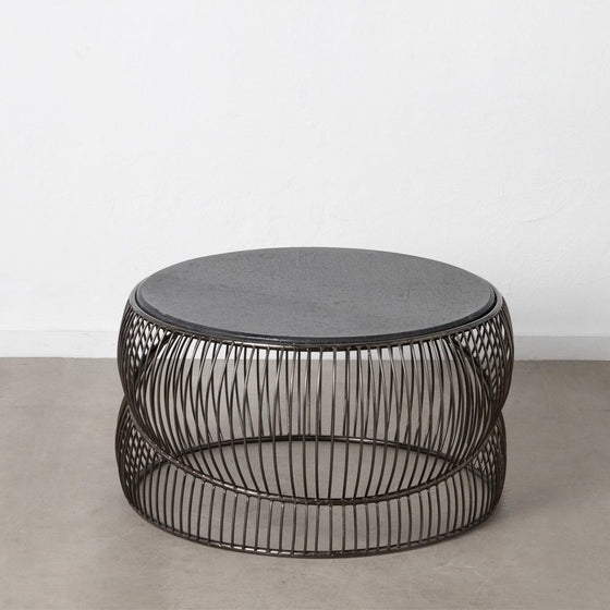 El elegante diseño de la Mesa de centro en metal y mármol plata Novax, con cubierta negra, se destaca sobre un piso de concreto contra una pared blanca nítida, exudando encanto minimalista y sofisticación moderna.